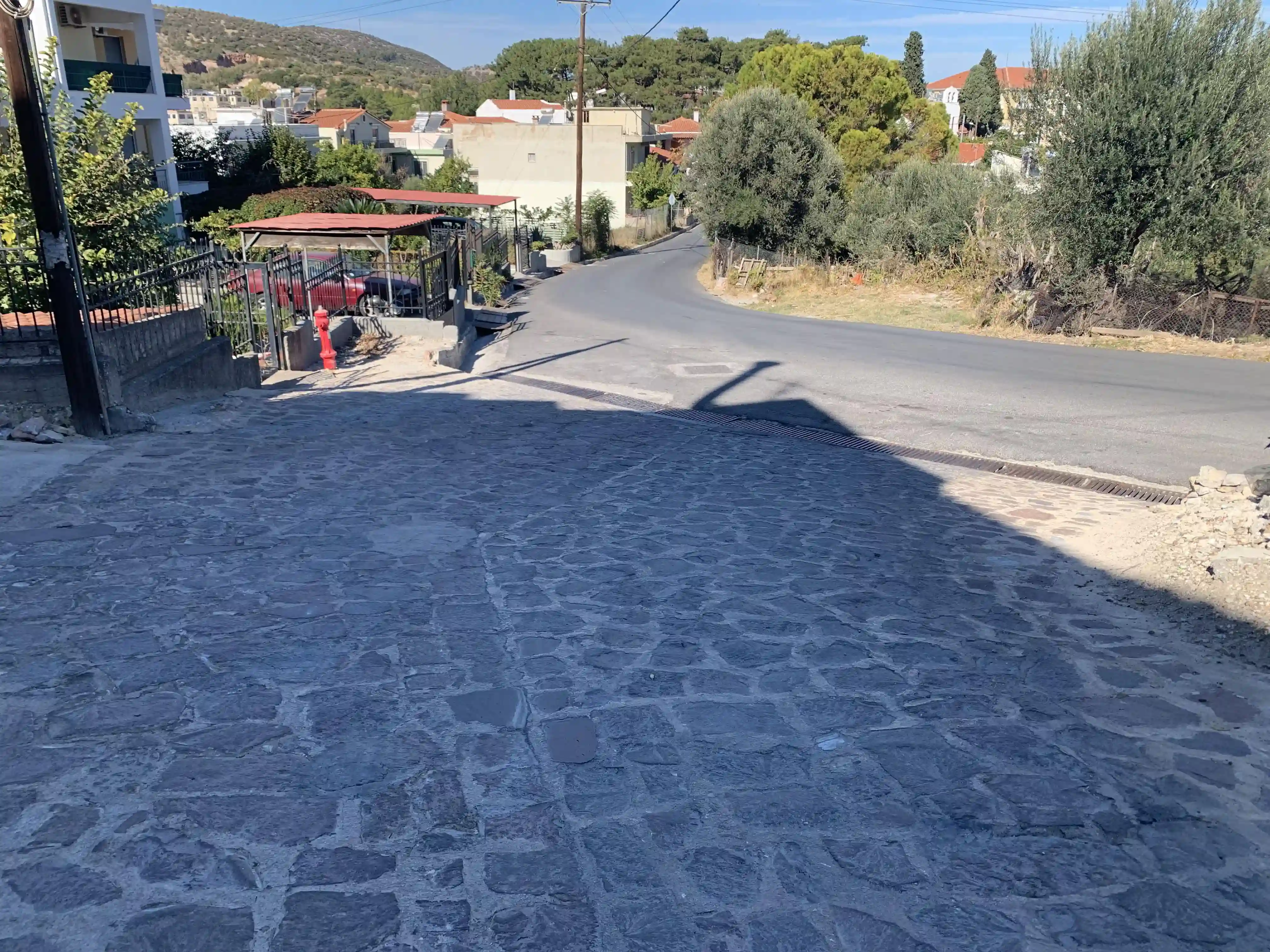 Απεικόνιση πλακόστρωτου κατηφορικού δρόμου εντός του Δήμου Μυτιλήνης στη περιοχή του Ακλειδιού, όπου στο τέλος του πλακόστρωτου έχει φρεάτια και εκεί συναντάει τον κεντρικό δρόμο.